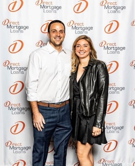 Man weareing white shirt and blue jeans woman wear black dress and leather jaclket stadning next to each other smiling 